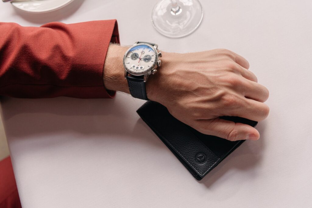 Mercedes-Benz Armbanduhr am Handgelenk mit schwarzer Ledergeldbörse auf einem gedeckten Tisch.